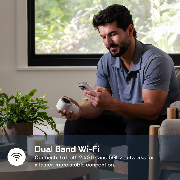 Man using a smartphone with a Dual Band Wi-Fi camera in a living room.
